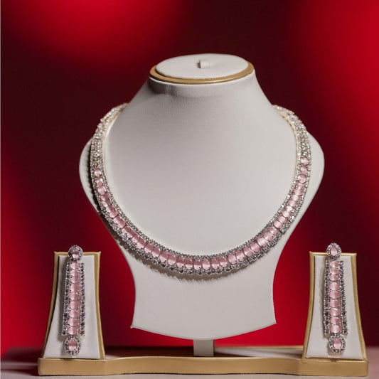 A dazzling pink and diamond statement necklace set with matching long drop earrings displayed on white jewelry busts against a vibrant red background.
