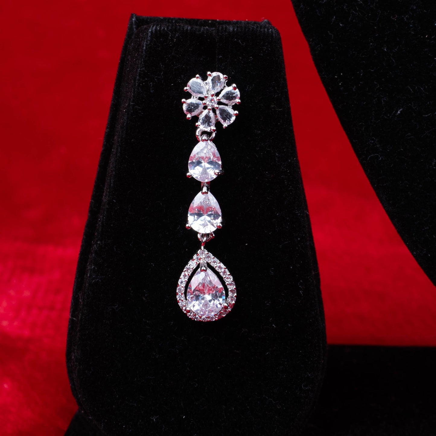 Diamond floral and teardrop dangle earring on black velvet with red background