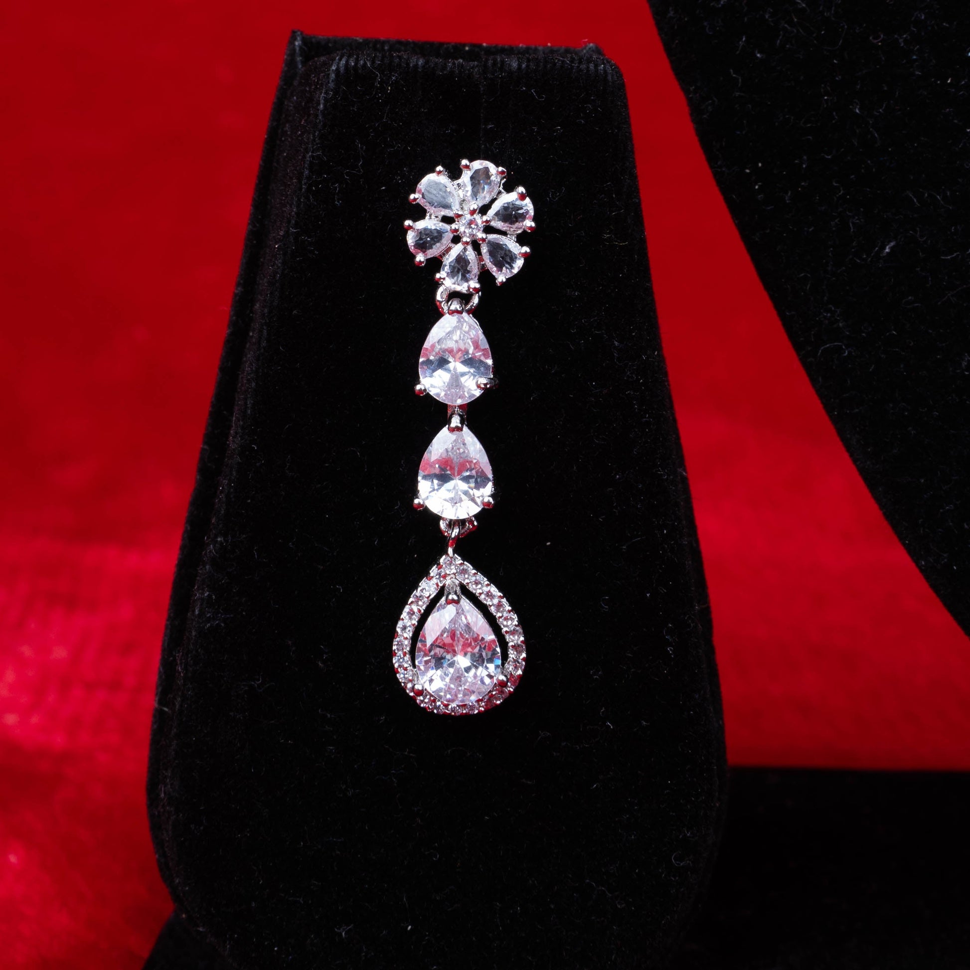 Diamond floral and teardrop dangle earring on black velvet with red background