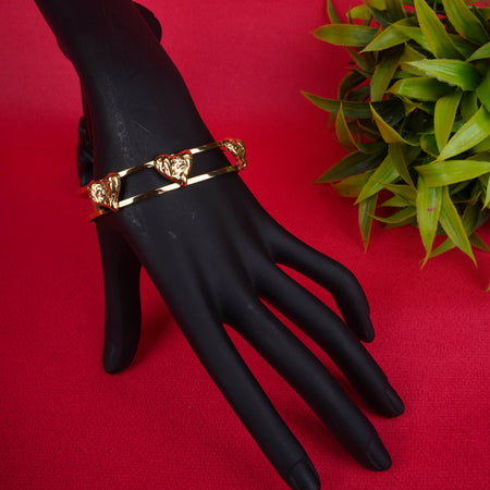 Gold-tone open cuff bracelet with three heart motifs on a black display hand - Revaaj