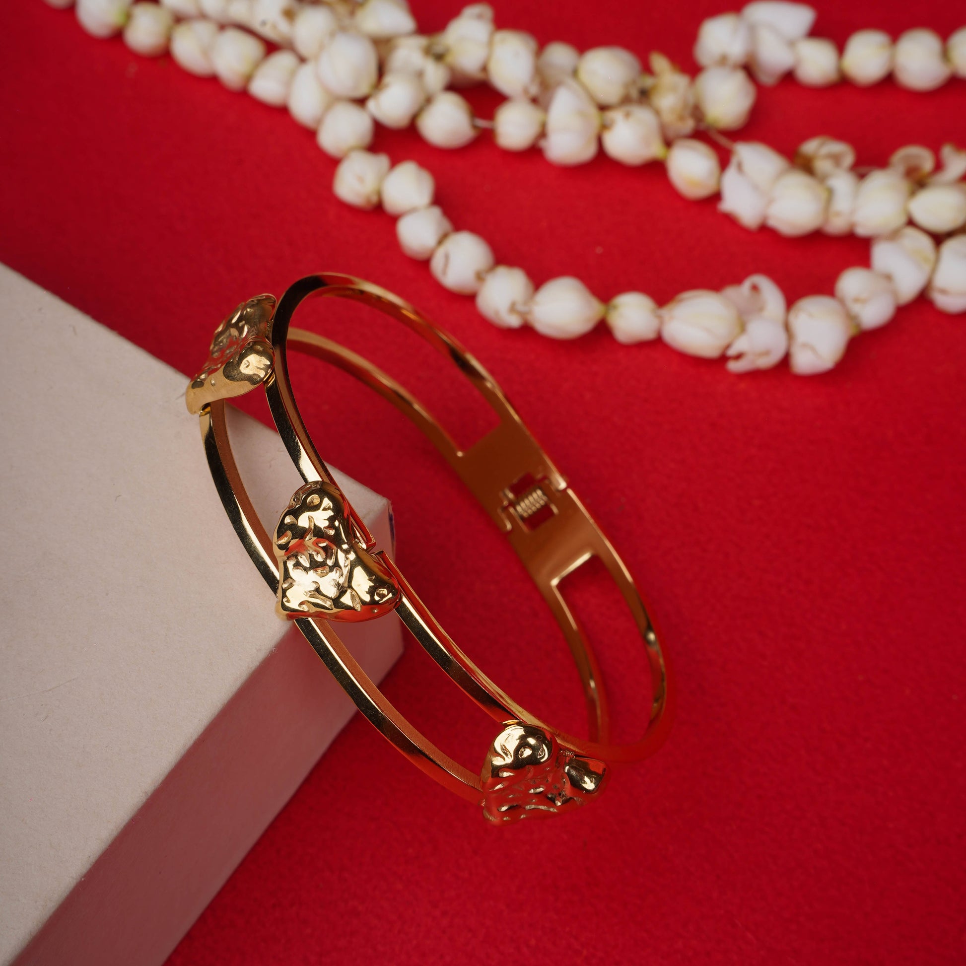 Gold-tone open cuff bracelet with three heart motifs on a black display hand - Revaaj Ground