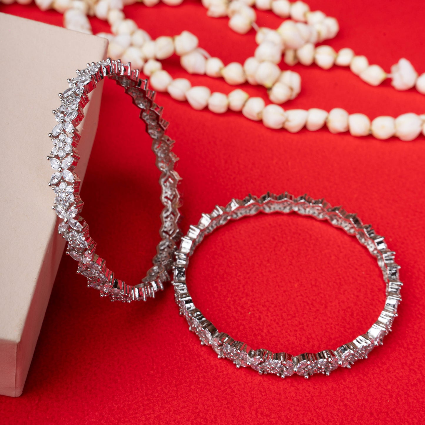 Silver floral vine stone bangle displayed on a black mannequin hand with red background - Revaaj Ground