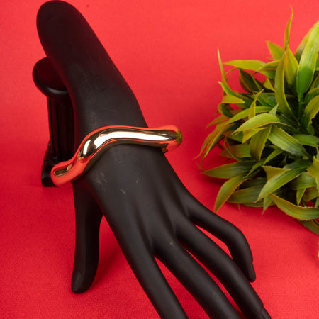 Gold wave-shaped bangle bracelet on a black mannequin hand - Revaaj