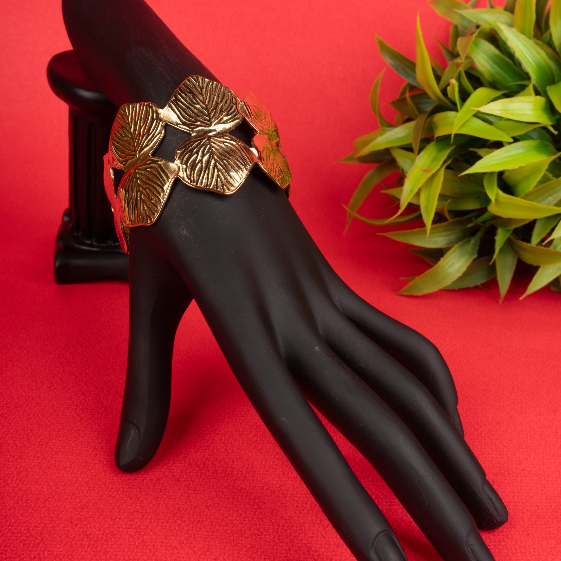 Wide gold-tone cuff bracelet with interlocking leaf motifs on a black mannequin hand - Revaaj