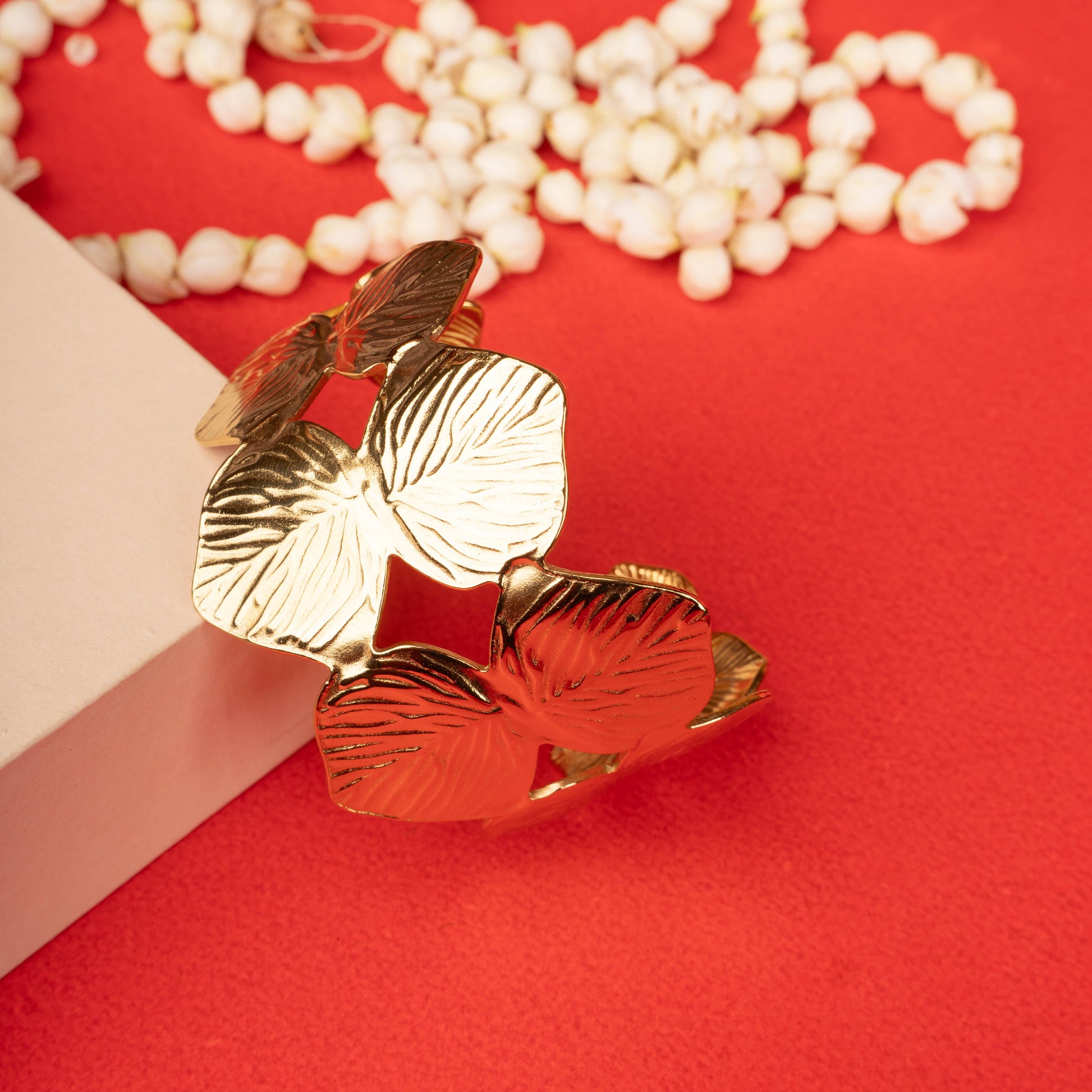 Wide gold-tone cuff bracelet with interlocking leaf motifs on a black mannequin hand ground image - Revaaj