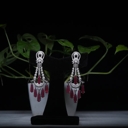 Ruby red chandbali earrings with crystal accents displayed on black stand