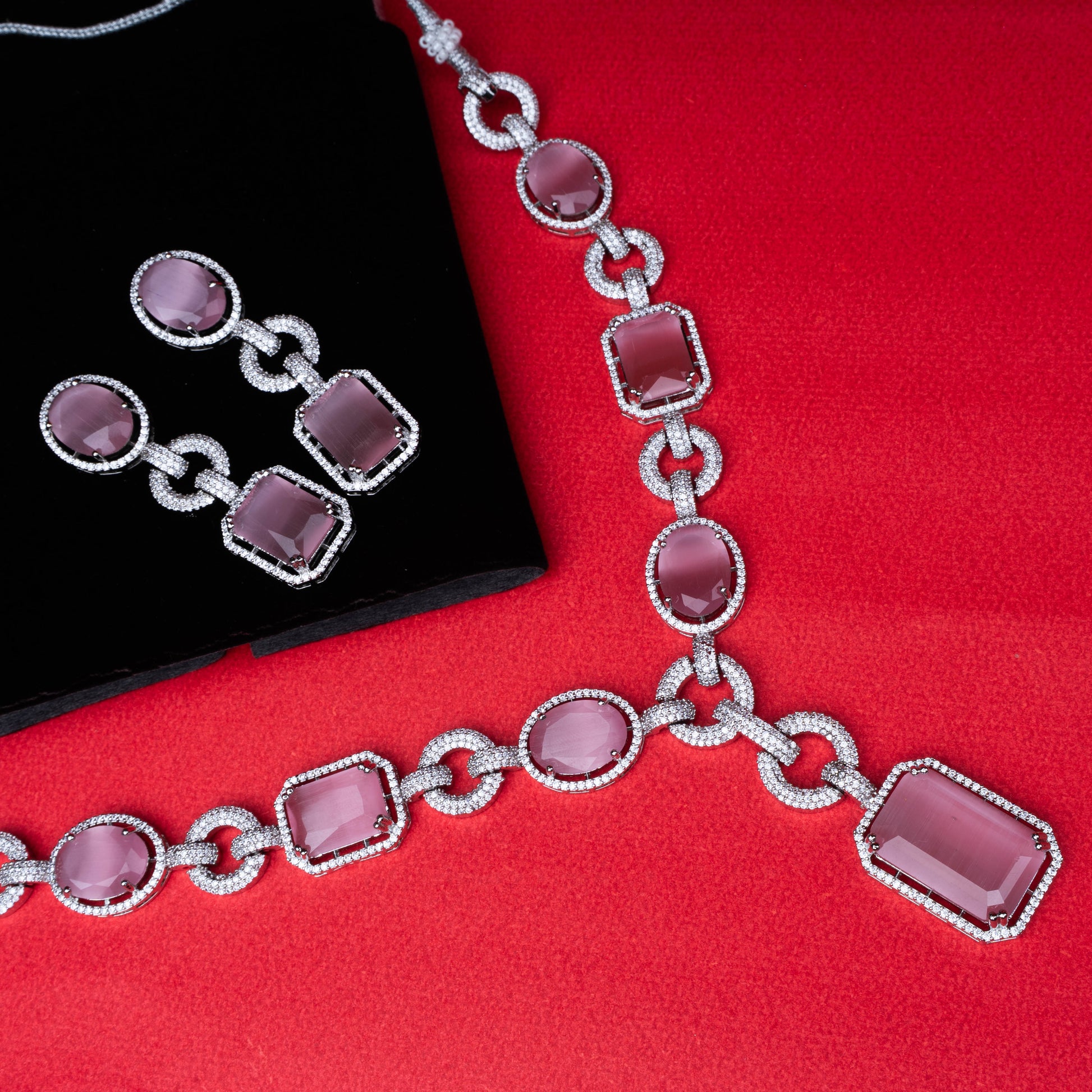Silver necklace and earring set with large pink gemstones and circular chain links on red background