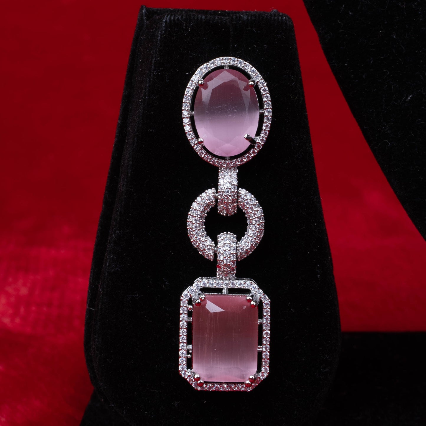 Silver drop earring with oval and rectangular pink gemstones on black velvet with red background