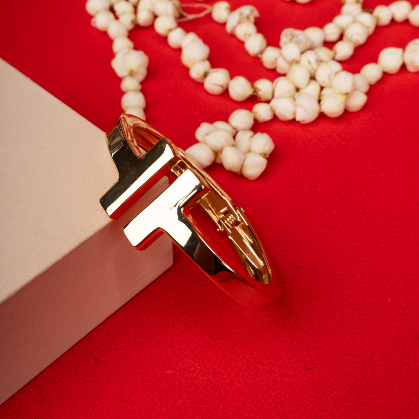 Gold-tone T-bar hinged bangle bracelet on a ground background - Revaaj