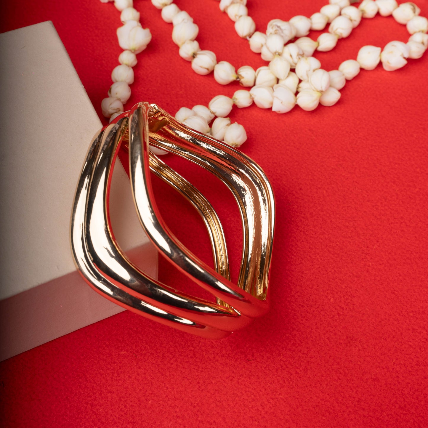 Gold-tone open cuff bracelet with a triple wave design, worn on a black mannequin hand ground image - Revaaj