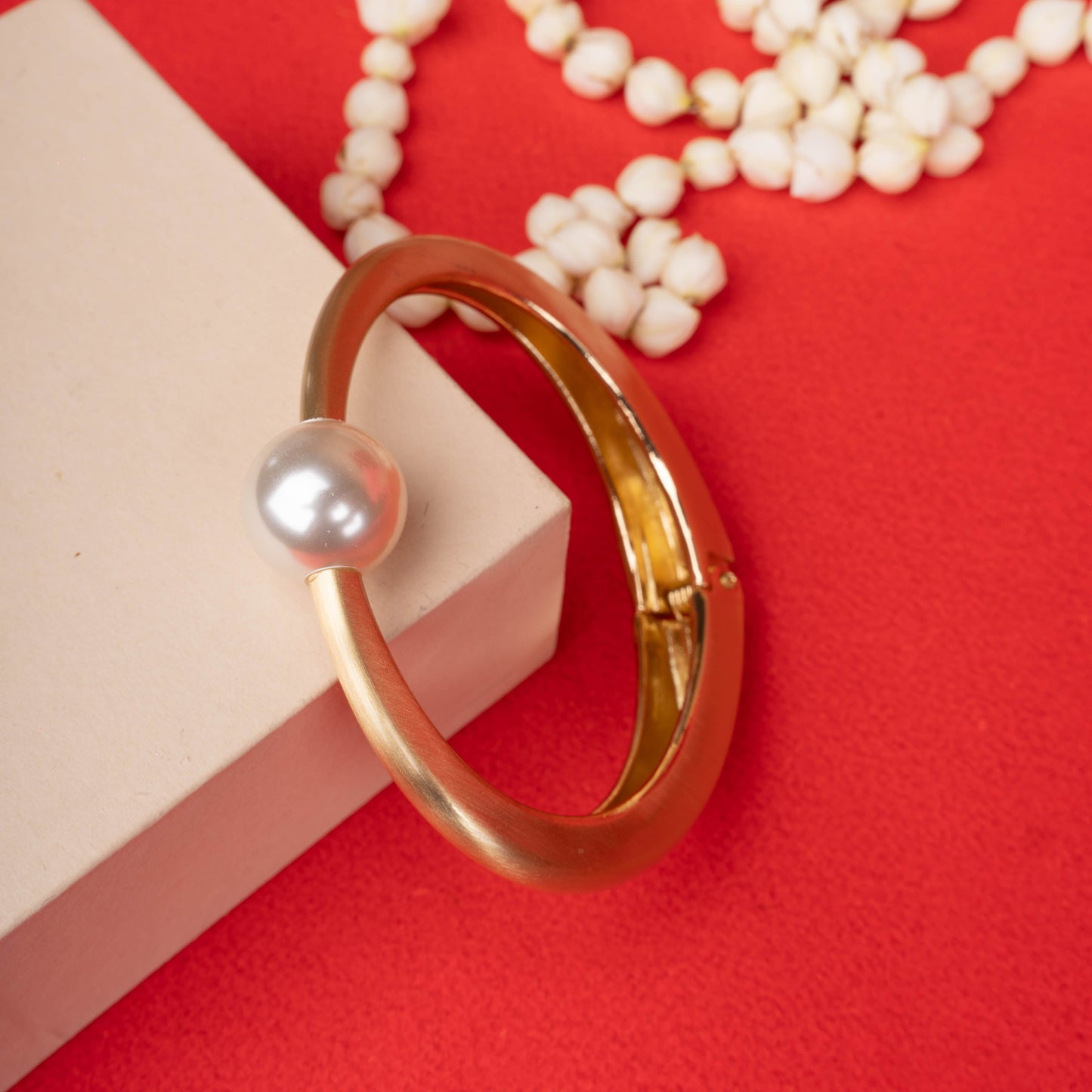 Gold-tone matte finish bangle bracelet with a single, large white pearl at the center in ground image  - Revaaj