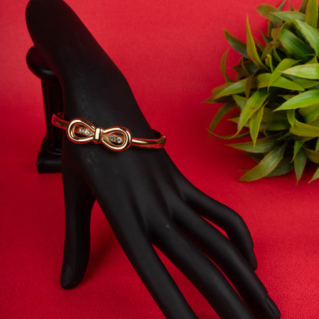 Gold-tone hinged bangle bracelet with a bow-shaped central motif encrusted with small crystals - Revaaj