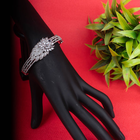 Ornate silver-tone hinged bracelet with a large, sparkling floral cluster made of clear crystals, and a band decorated with three rows of crystals and heart-shaped cutouts - Revaaj