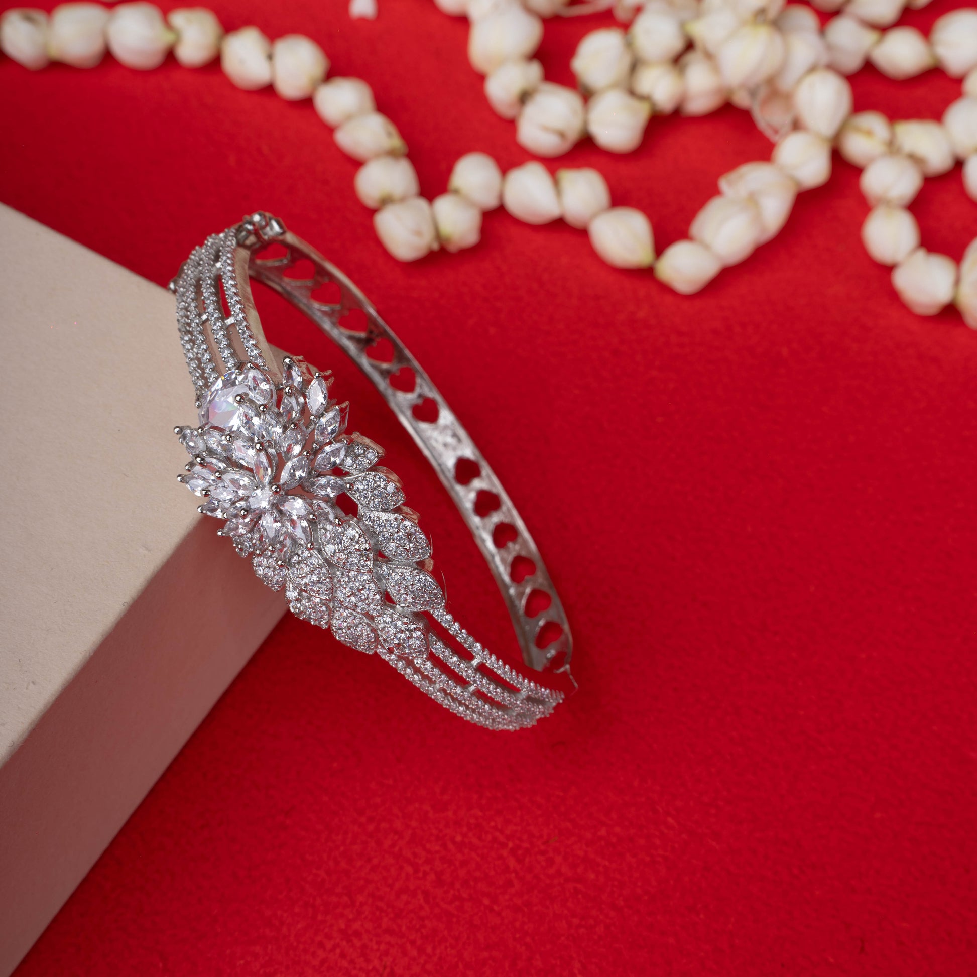 Ornate silver-tone hinged bracelet with a large, sparkling floral cluster made of clear crystals, and a band decorated with three rows of crystals and heart-shaped cutouts ground image - Revaaj
