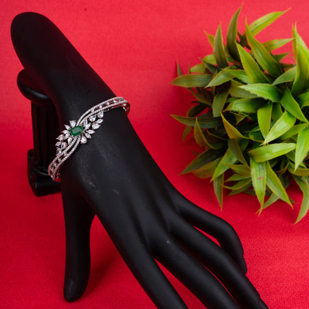 Silver-tone hinged bracelet with a prominent emerald-cut green gemstone at its center, surrounded by clear marquise and round crystals, and a band paved with micro-crystals ground image - Revaaj