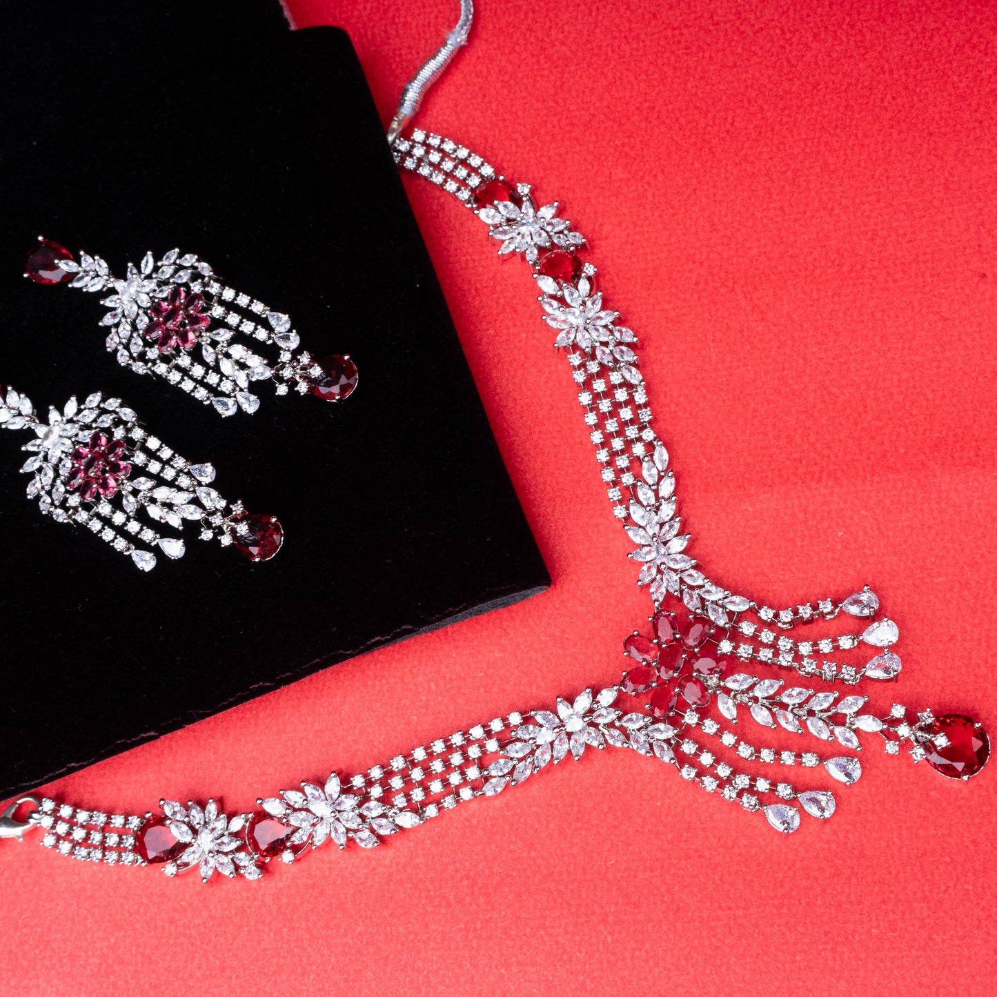 Necklace and earring set with red teardrop stones, floral motifs, and clear stone accents on red background