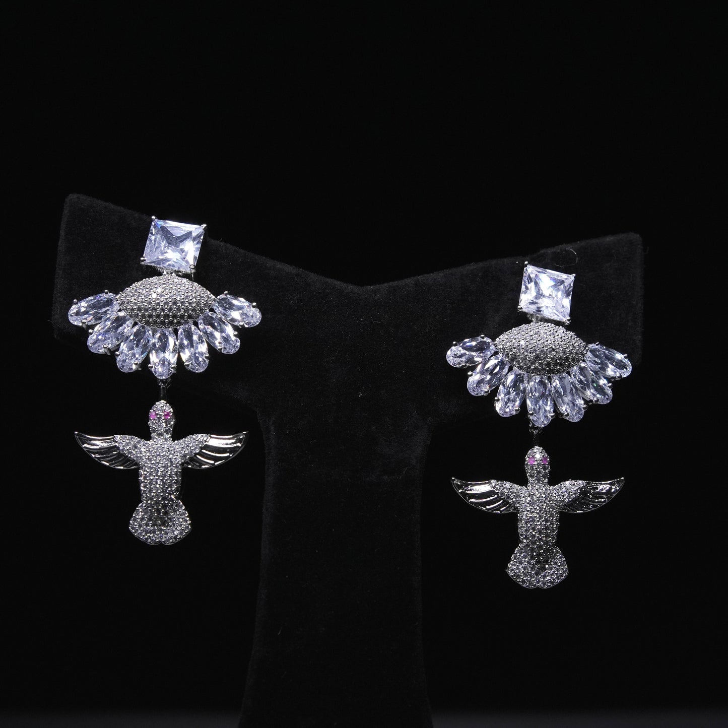 Angel wing designer earrings with crystal embellishments and square-cut stones displayed on black stand