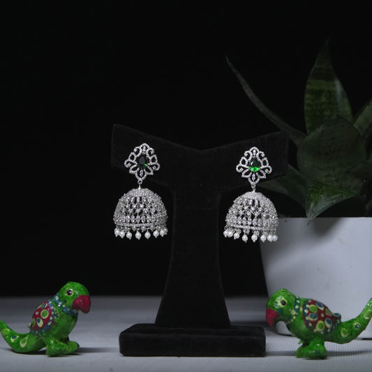 Classic CZ jhumka earrings with green stone accent displayed on black stand