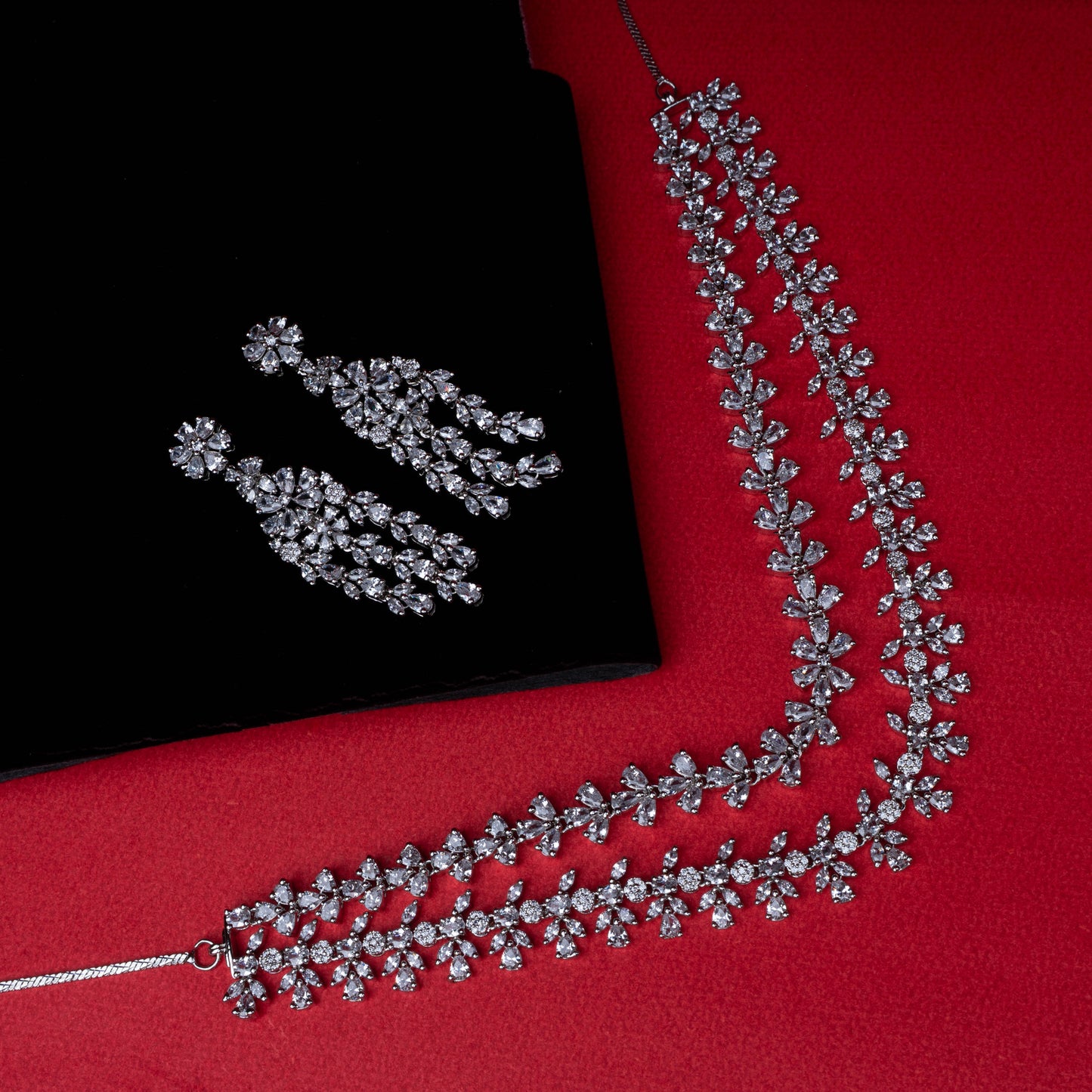 Necklace and earring set with floral motif clear stones in cascading design on red background