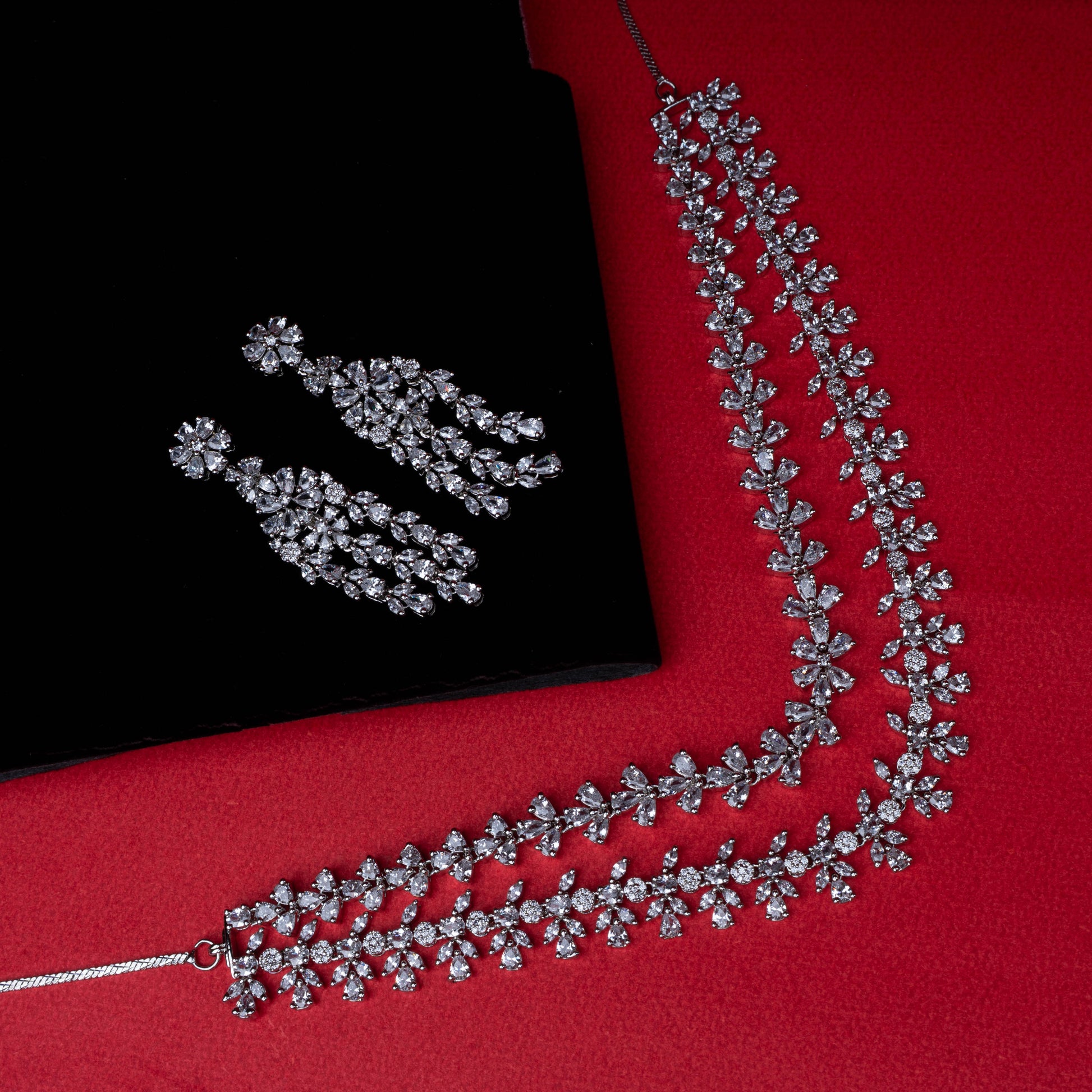 Necklace and earring set with floral motif clear stones in cascading design on red background