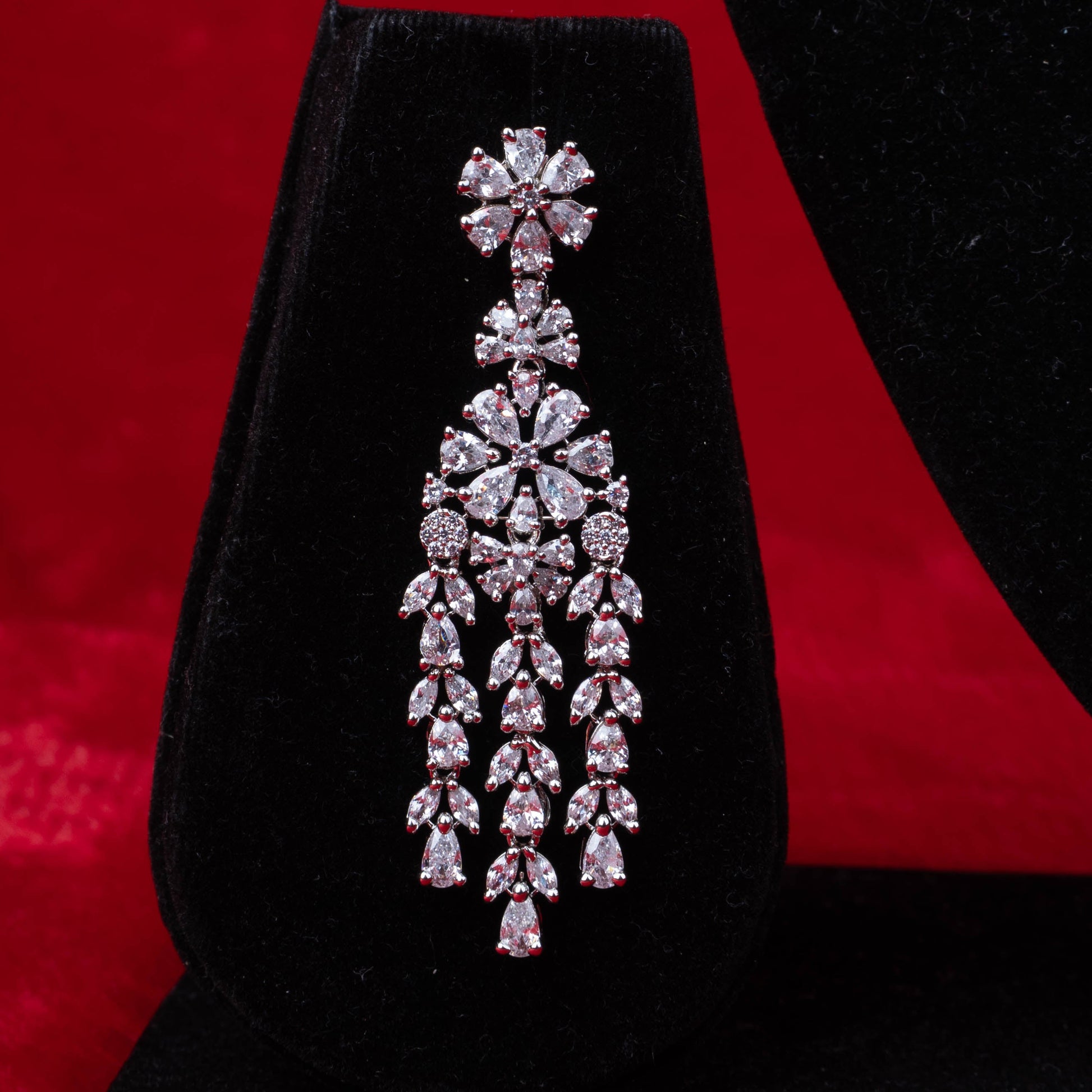 Earring with floral motif clear stones and cascading layered design on black velvet with red background