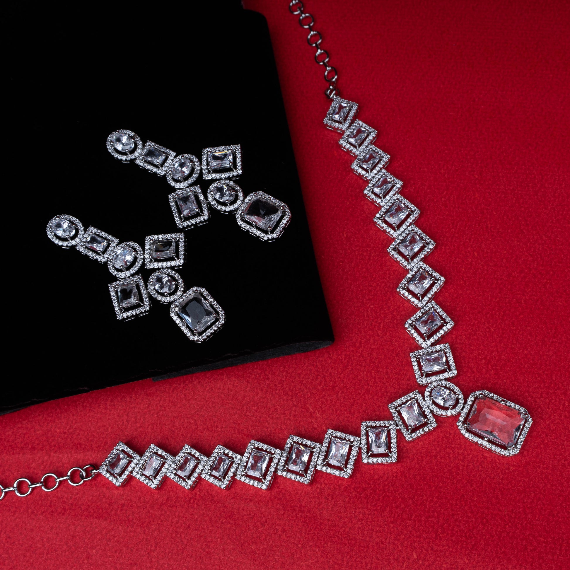 Necklace and earring set with square and round clear stones in halo design on red background