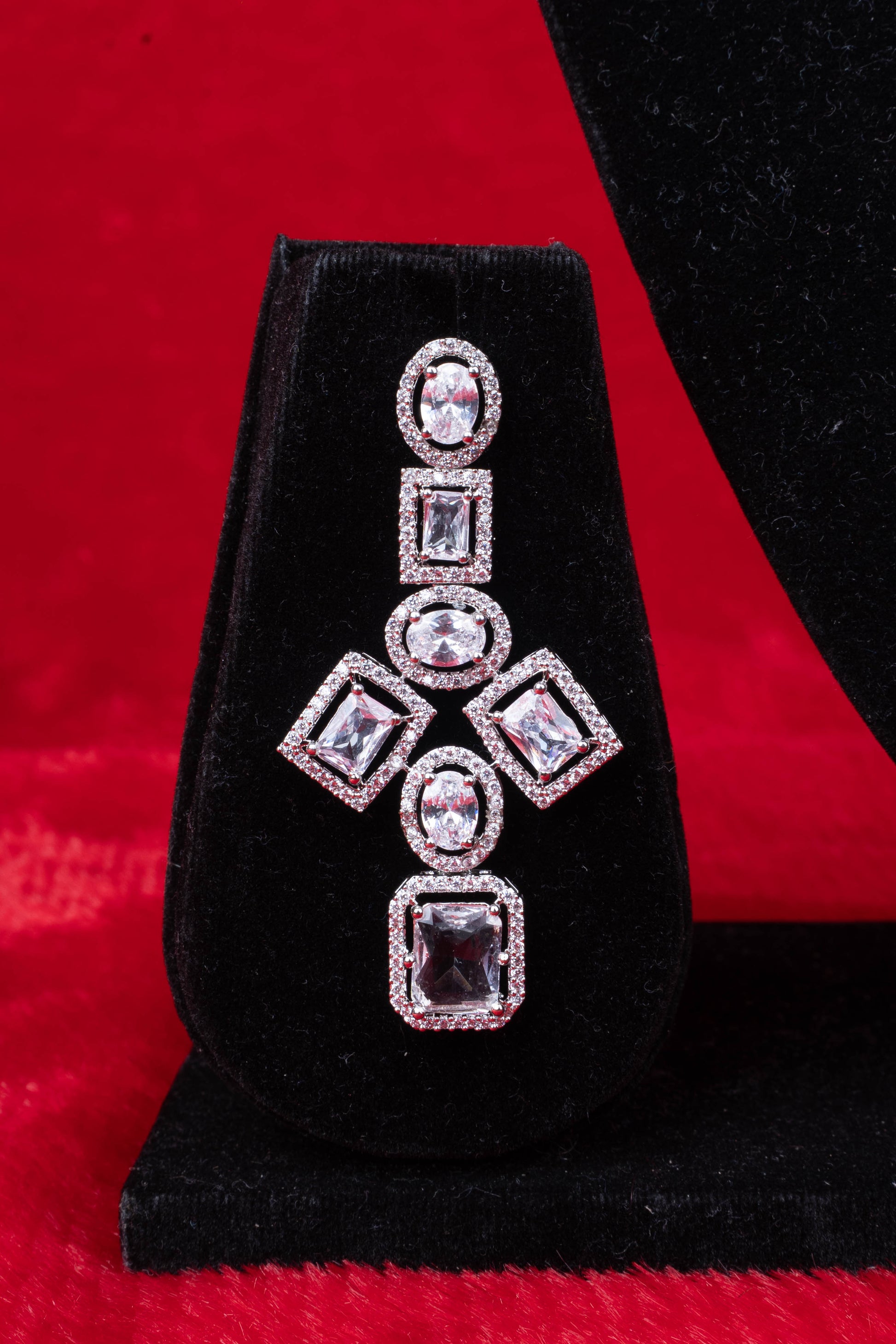 Earring with square and oval clear stones in halo setting on black velvet with red background