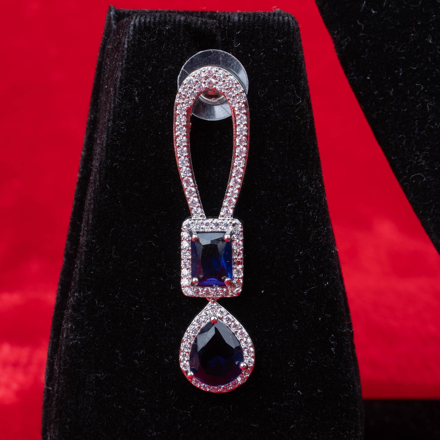 Earring with blue rectangular and teardrop stones in halo setting on black velvet with red background