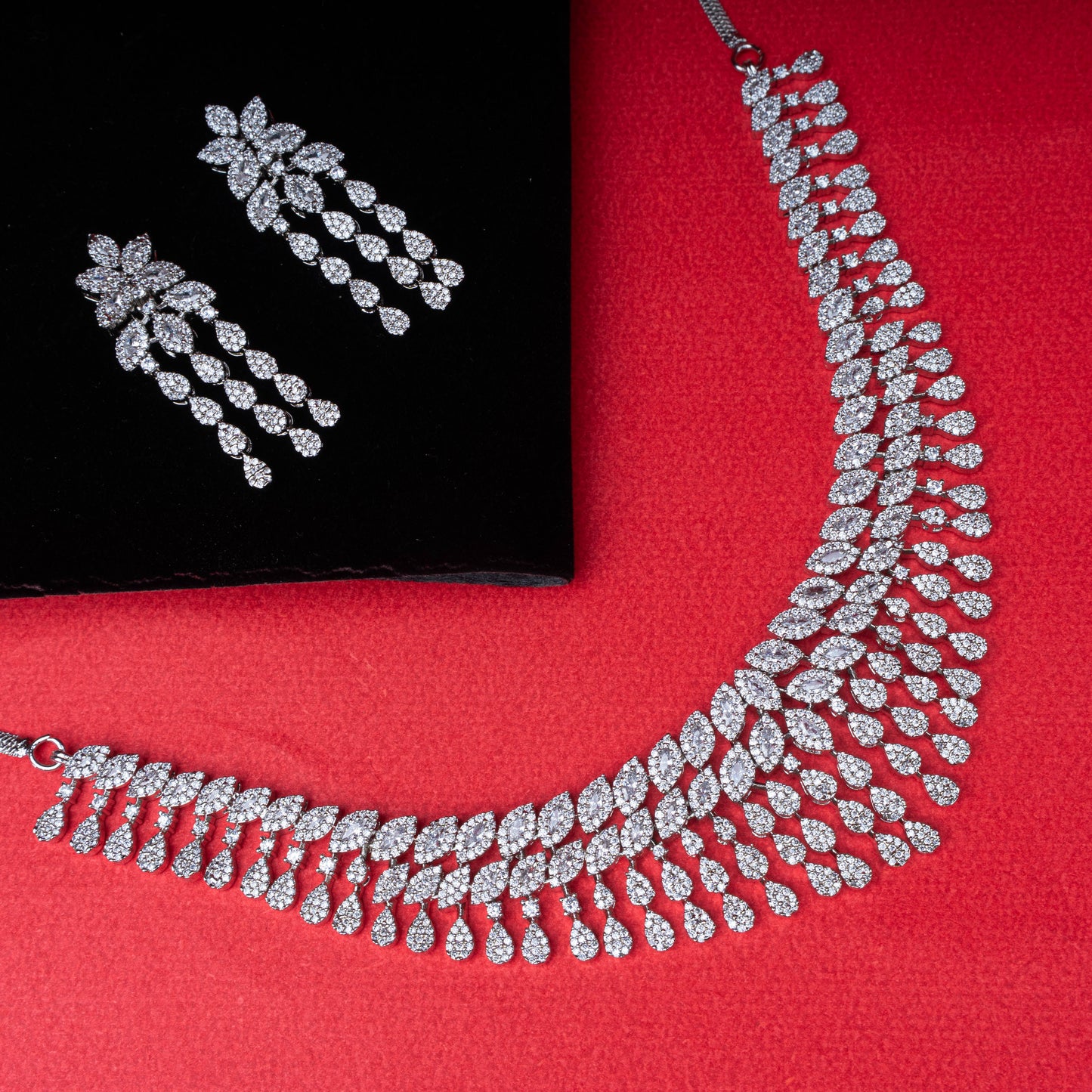 Floral and teardrop stone necklace and earring set in silver-tone setting on red background