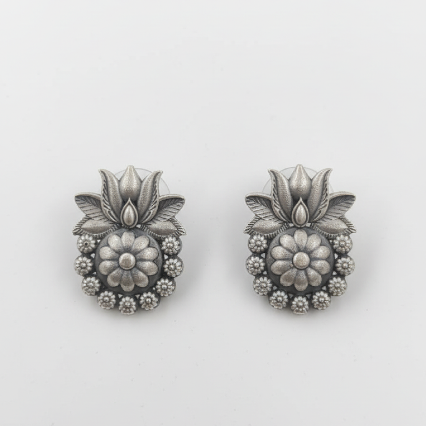 Oxidized silver floral stud earrings with intricate design displayed on a black stand ground