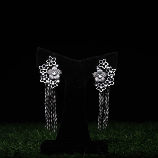 Oxidized silver floral tassel earrings with pearl accents and cascading chains displayed on black stand