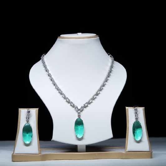Revaaj Emerald Green and White Cubic Zirconia Necklace and Earring Set displayed on a white jewelry stand against a black background.