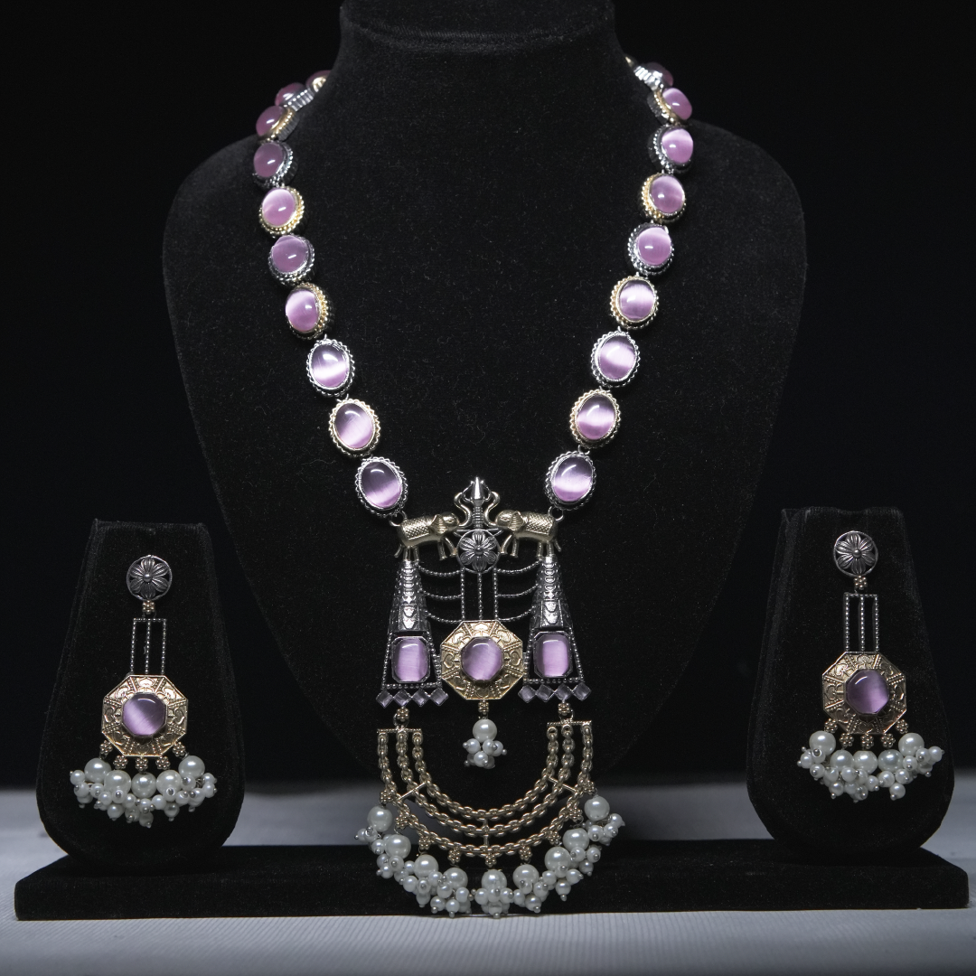 Revaaj Kundan necklace set with lavender gemstones and pearl earrings displayed on a black jewelry stand.
