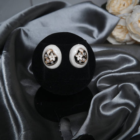 White enamel floral stud earrings with pearl and cubic zirconia accents, oval design displayed on a black velvet stand with silk background