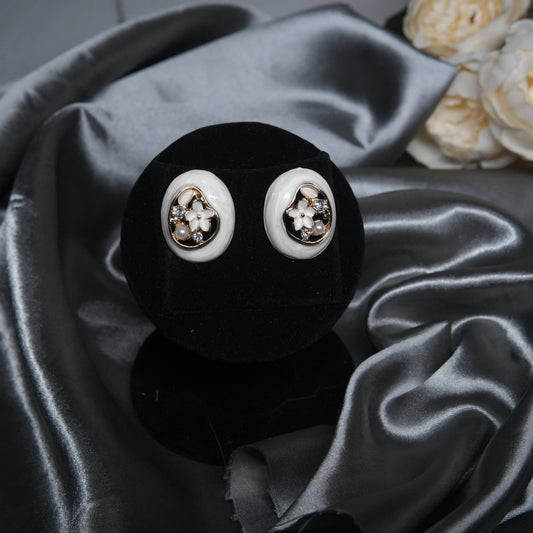 White enamel floral stud earrings with pearl and cubic zirconia accents, oval design displayed on a black velvet stand with silk background