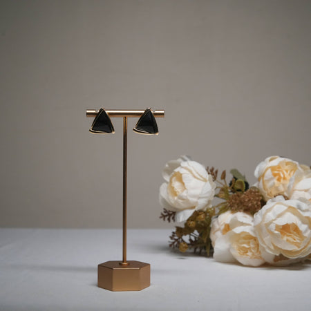 Minimalist black triangle stud earrings in gold finish displayed on a golden stand