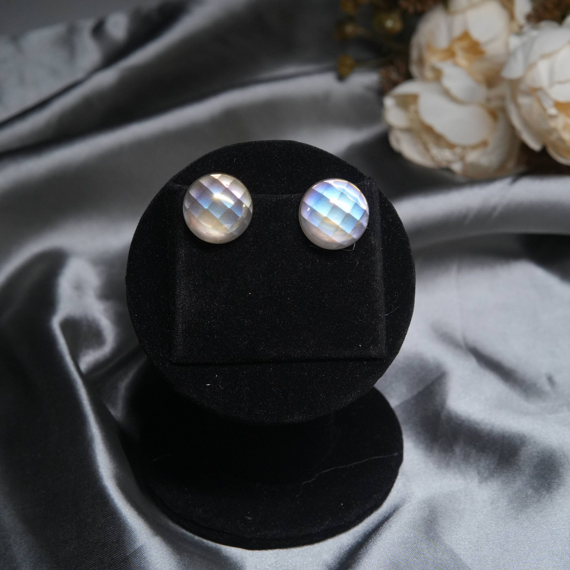 Moonstone stud earrings with polished silver frame displayed on black velvet stand.