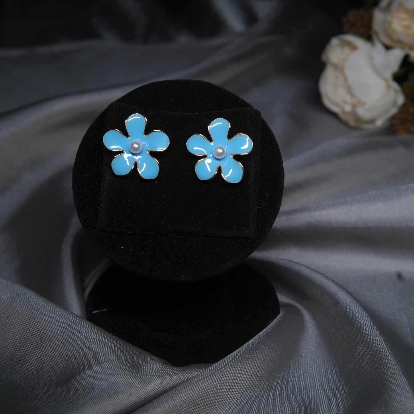 Sky blue floral enamel stud earrings with pearl center displayed on black velvet stand.