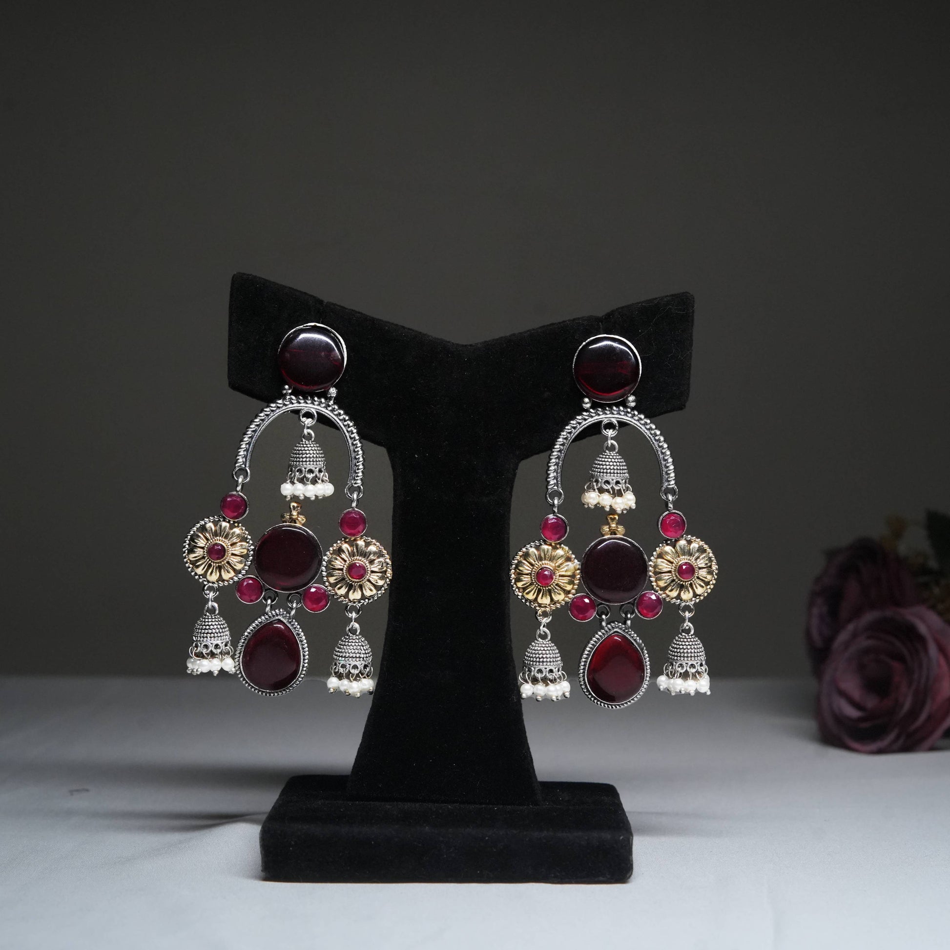 Antique red & gold temple jhumka earrings with ruby beads displayed on golden stand.