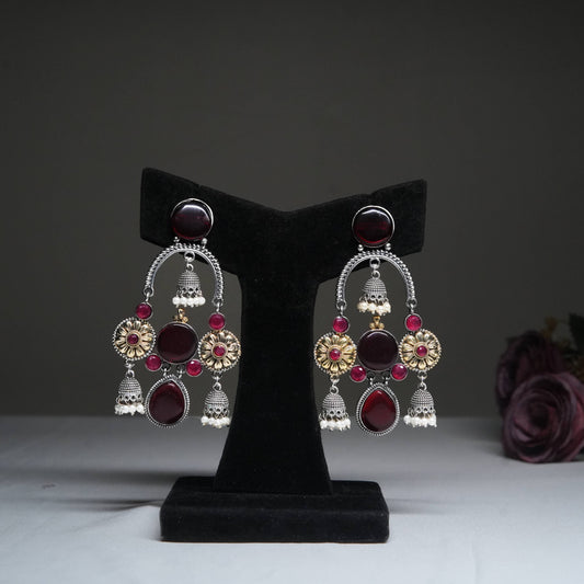 Antique red & gold temple jhumka earrings with ruby beads displayed on golden stand.