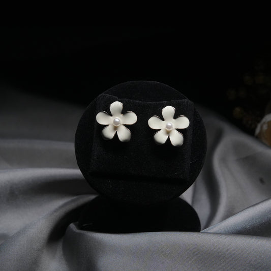 White enamel floral stud earrings with pearl center displayed on black velvet stand.