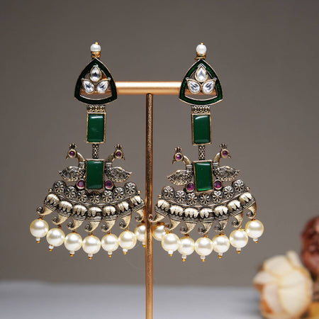 Green enamel peacock jhumka earrings with kundan stones and pearl hangings displayed on a golden stand.