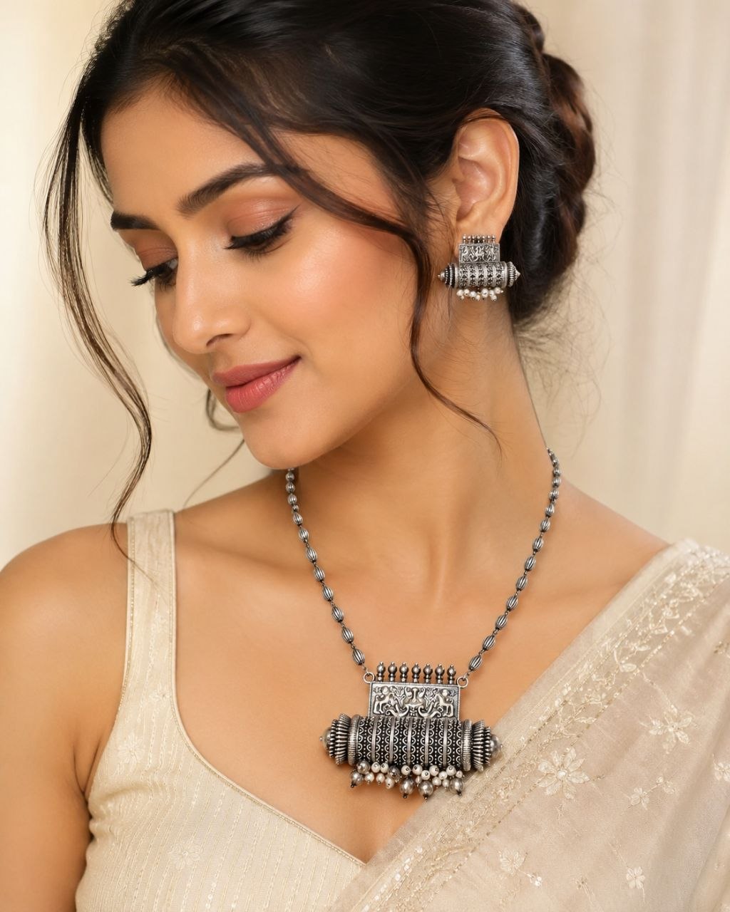 Oxidized silver necklace with detailed elephant pendant and dangling pearl beads paired with matching earrings on beige background 2