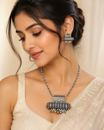 Oxidized silver necklace with detailed elephant pendant and dangling pearl beads paired with matching earrings on beige background 2