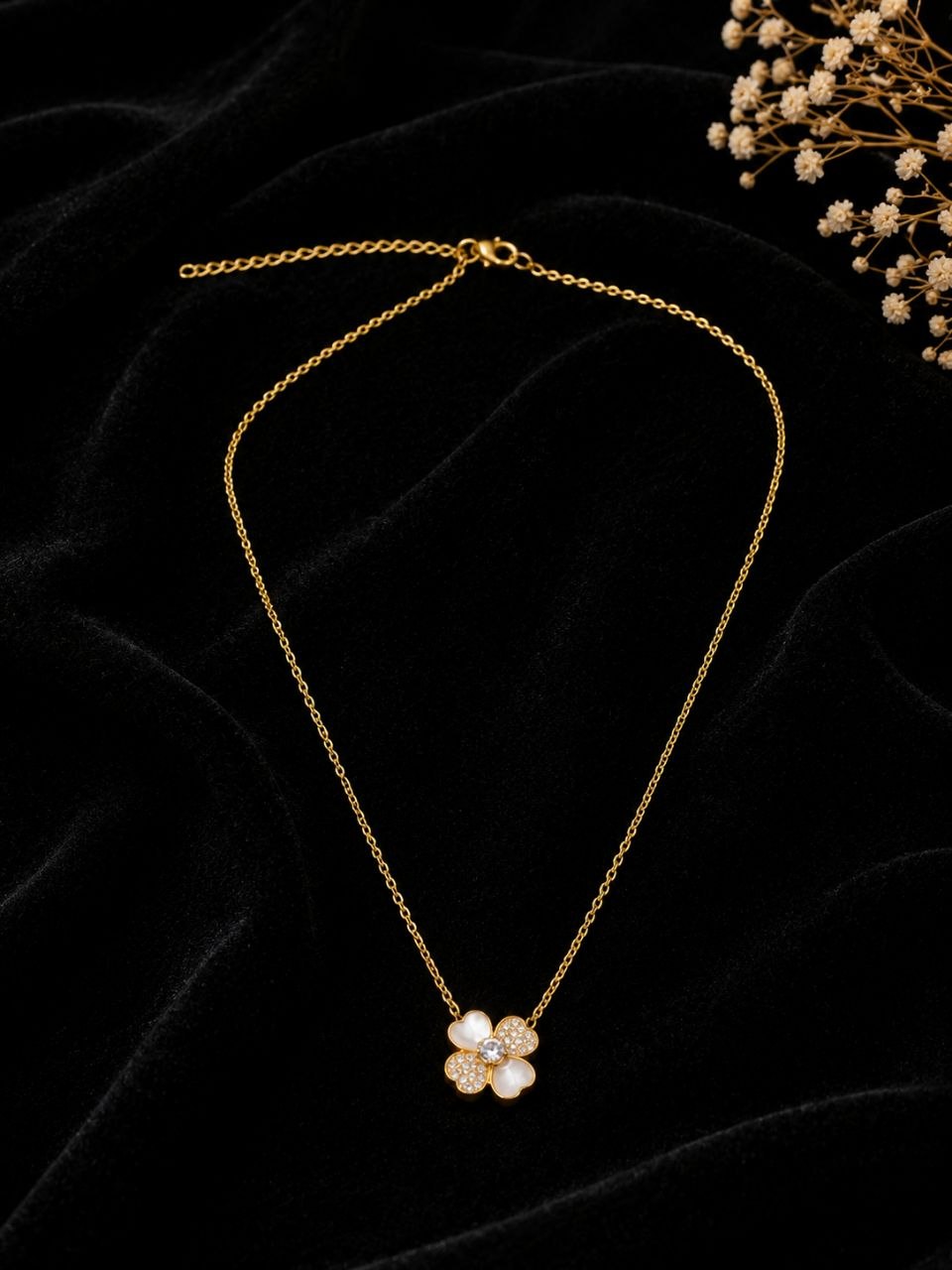Delicate gold chain necklace with white four-petal floral pendant featuring sparkling crystal stones on beige background 3