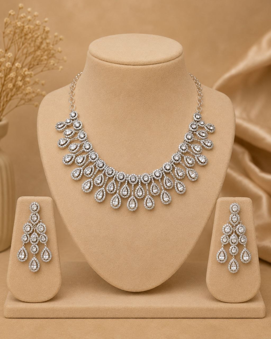 Luxury silver teardrop American diamond necklace and matching earrings set displayed on beige jewelry bust with soft beige background 1