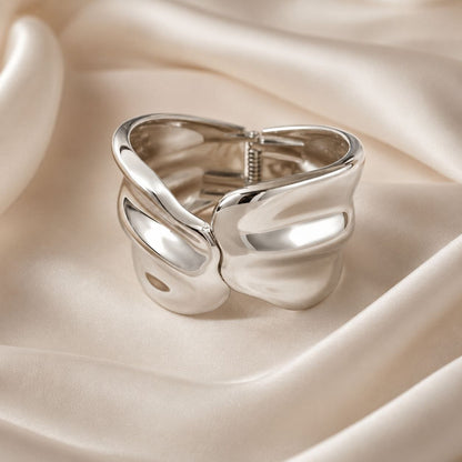 Polished silver abstract wavy sculptural statement ring displayed on soft beige silk fabric 1