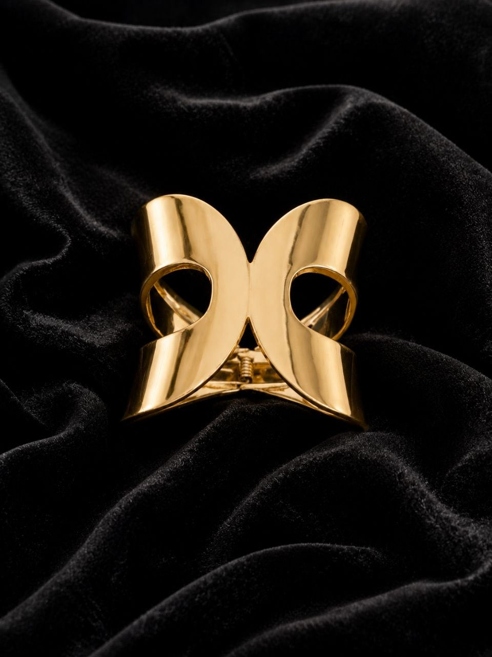 Shiny gold bow-shaped metallic hair claw clip displayed on white satin fabric 3