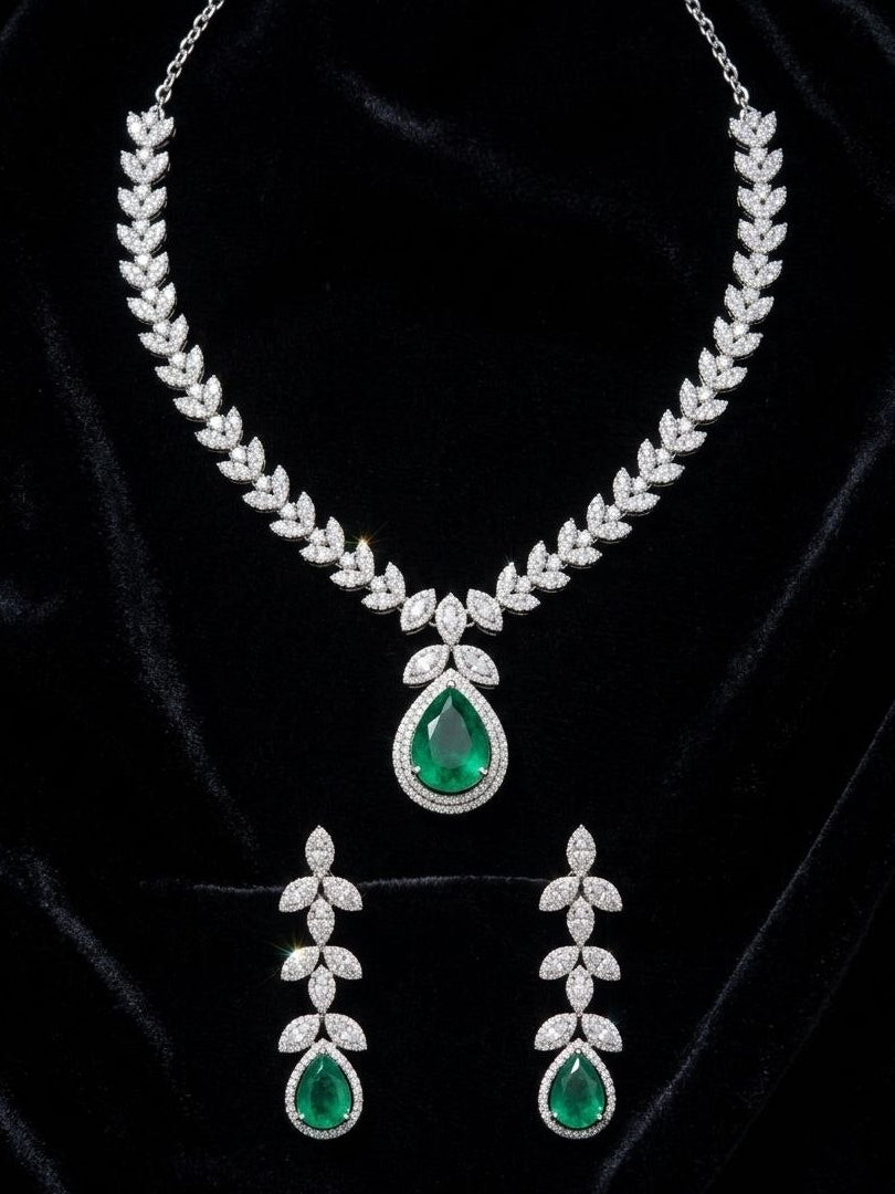 Luxury silver necklace with large green emerald teardrop pendant and matching dangling earrings featuring leaf motif cubic zirconia stones on white fabric 3