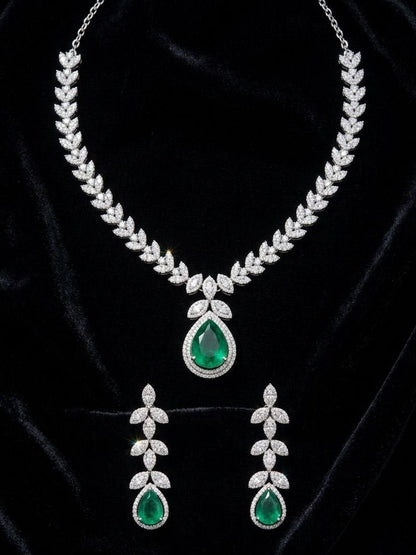Luxury silver necklace with large green emerald teardrop pendant and matching dangling earrings featuring leaf motif cubic zirconia stones on white fabric 3